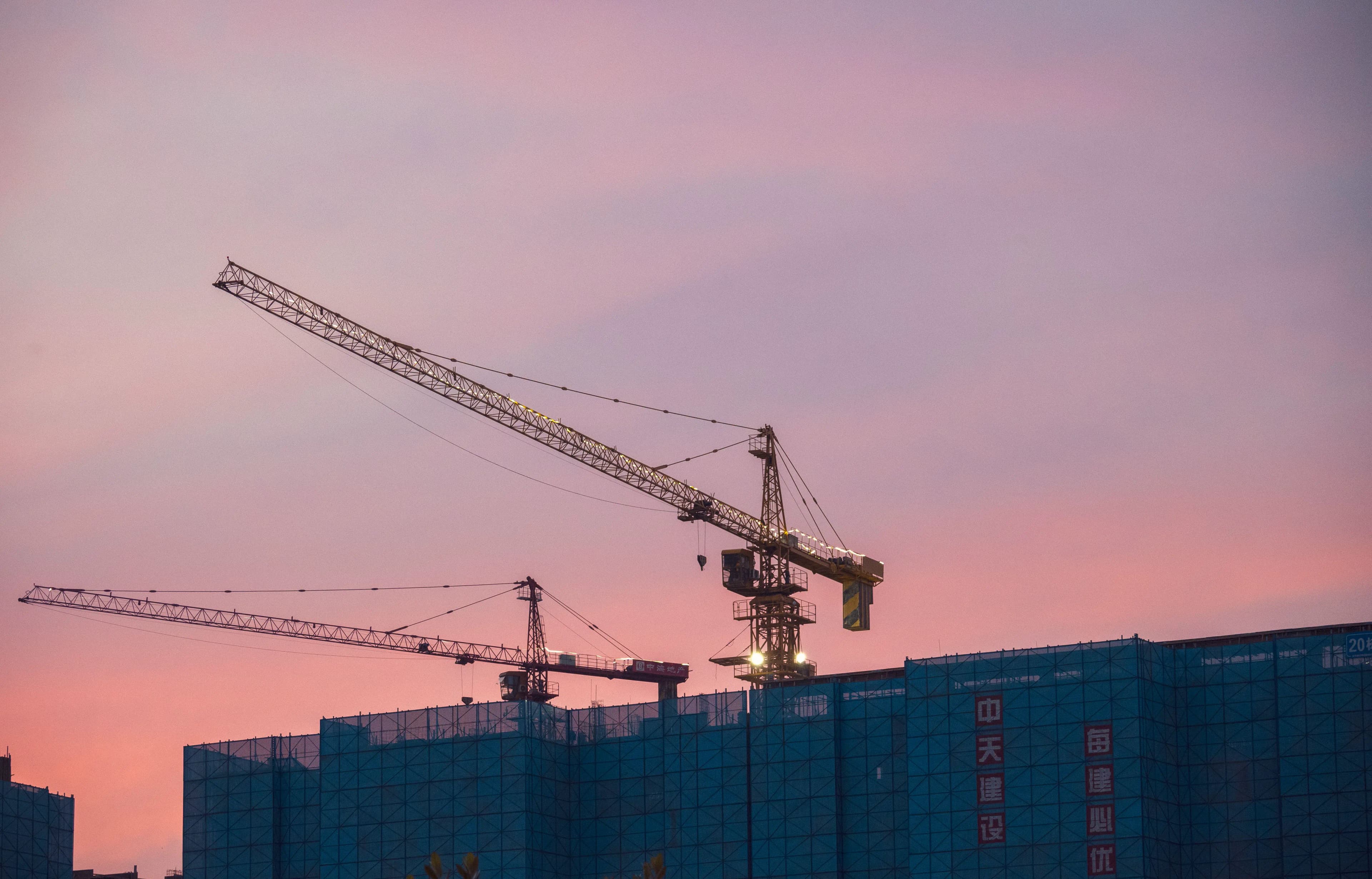 Tower cranes above a building under construction at sunset